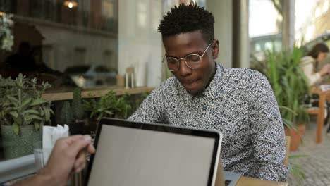 Hombre-Afroamericano-Sonriente-Usando-Una-Computadora-Portátil-En-La-Cafetería